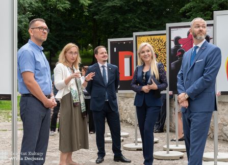 fotografia. art piknik w willi decjusza. plenerowa wystawa plakatów teatralnych. grupa ludzi przed plakatami ustawionymi w rzędach po dwóch stronach żwirowej alejki.